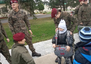 Dzieci w obecności żołnierzy oglądają i przymierzają spadochron.