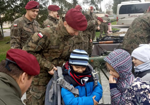 Dzieci w obecności żołnierzy oglądają i przymierzają spadochron.