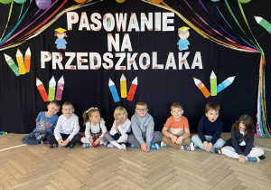Zdjęcie grupowe na tle dekoracji z okazji Pasowania na przedszkolaka.
