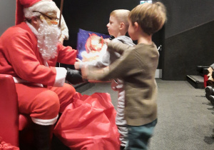 Dzieci odbierają prezent od Mikołaja.