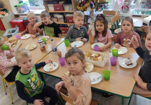 Dzieci siedzą przy stoliku i zajadają pyszności.