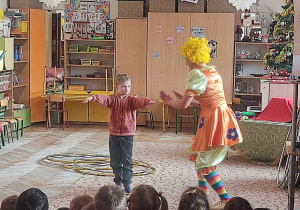 Chłopiec wykonuje ćwiczenia zaproponowane przez klauna.