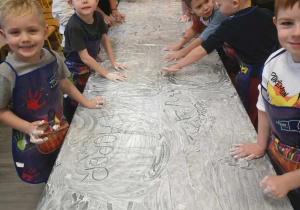 Dzieci malują rączkami na folii pełnej białej farby.
