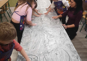 Dzieci malują rączkami na folii pełnej białej farby.