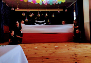 Dziewczynki ubrane na czarno tańczą z flagami polski.
