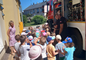 Dzieci z strażakami na tle ich pojazdu.