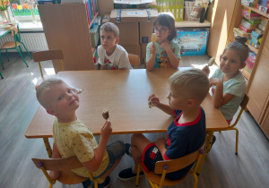 Dzieci siedzą przy stolikach i jedzą lody.