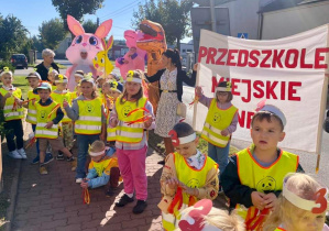 Dzieci idą korowodem w odblaskowych kamizelkach.