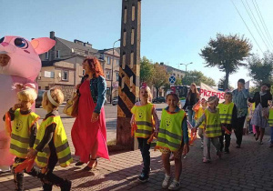 Dzieci maszerują ulicami miasta świętując dzień przedszkolaka.