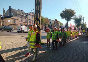 Dzieci maszerują ulicami miasta świętując dzień przedszkolaka.