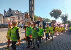 Dzieci maszerują ulicami miasta świętując dzień przedszkolaka.