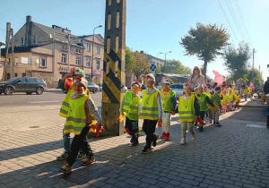 Dzieci maszerują ulicami miasta świętując dzień przedszkolaka.