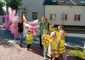 Dzieci maszerują ulicami miasta świętując dzień przedszkolaka.