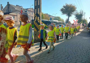 Dzieci maszerują ulicami miasta świętując dzień przedszkolaka.