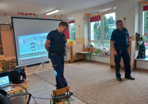 Policjanci na tle telebimu z bajką.