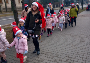 Dzieci z Mikołajem na przodzie, w czapkach mikołajkowych biorą udział w przemarszu ulicami Ozorkowa.