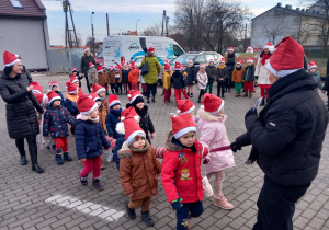 Dzieci z Mikołajem na przodzie, w czapkach mikołajkowych biorą udział w przemarszu ulicami Ozorkowa.