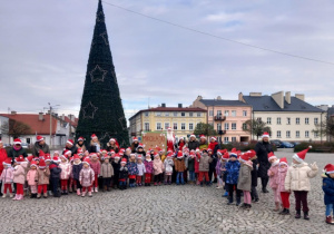 Zdjęcie grupowe z Mikołajem pod dużą choinką na rynku Ozorkowa.