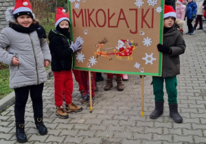 Dzieci z Mikołajem na przodzie, w czapkach mikołajkowych biorą udział w przemarszu ulicami Ozorkowa.