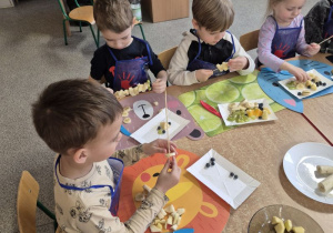 Dzieci przygotowują szaszłyki owocowe.
