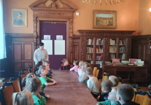 Dzieci siedzą przy dużym stole w bibliotece.
