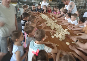 Dzieci przy dużym stole robią własne wypieki.