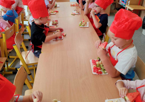 Dzieci jedzą owocowe szaszłyki.