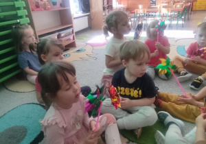Dzieci na dywanie dmuchają w wiatraczki.