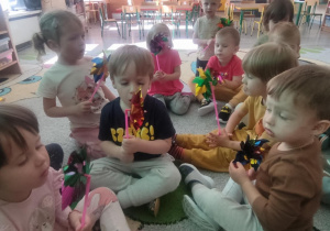 Dzieci na dywanie dmuchają w wiatraczki.