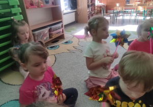 Dzieci na dywanie dmuchają w wiatraczki.
