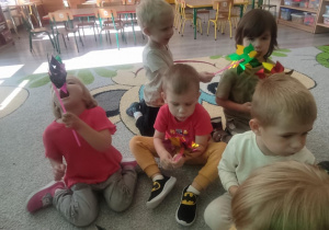 Dzieci na dywanie dmuchają w wiatraczki.