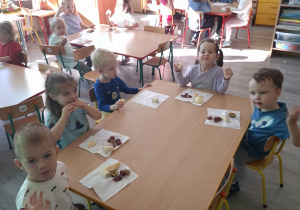 Dzieci przy stoliku spożywają owoce.