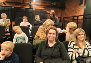 Dzieci siedzą na fotelach w teatrze i czekają na spektakl.