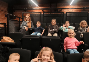 Dzieci siedzą na fotelach w teatrze i czekają na spektakl.