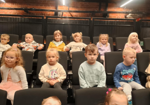 Dzieci siedzą na fotelach w teatrze i czekają na spektakl.