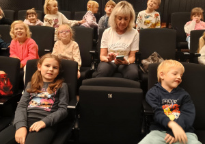 Dzieci siedzą na fotelach w teatrze i czekają na spektakl.