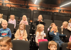 Dzieci siedzą na fotelach w teatrze i czekają na spektakl.
