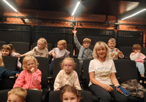 Dzieci siedzą na fotelach w teatrze i czekają na spektakl.
