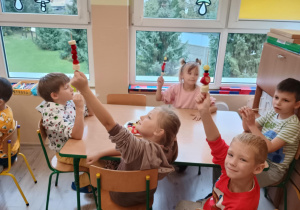 Dzieci przy stoliku siedzą z szaszłykami w rączkach.