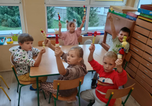 Dzieci przy stoliku siedzą z szaszłykami w rączkach.