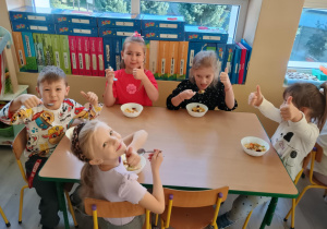 Dzieci przy stolikach kroją owoce na sałatkę.