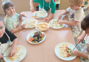 Dzieci przy stolikach kroją owoce na sałatkę.