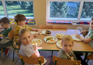 Dzieci przy stolikach kroją owoce na sałatkę.