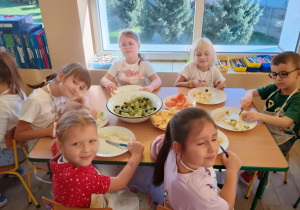 Dzieci przy stolikach kroją owoce na sałatkę.