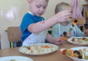 Dzieci przy stolikach robią szaszłyki.