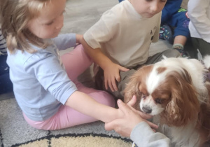 Piesek liże dzieci po paluszku posmarowanym smakołykiem.