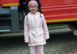 Dziecko w kasku strażackim na tle samochodu strażackiego.