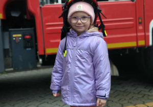 Dziecko w kasku strażackim na tle samochodu strażackiego.