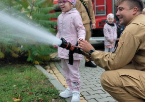 Dziecko wraz z strażakiem leje wodę w prądownicy.