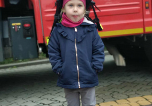 Dziecko w kasku strażackim na tle samochodu strażackiego.